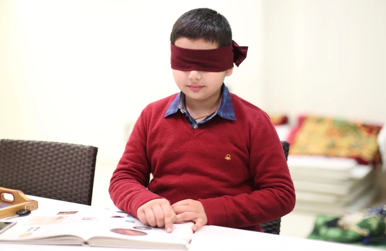 A blindfolded boy reading a picture book with his fingertips during the Intuition Process